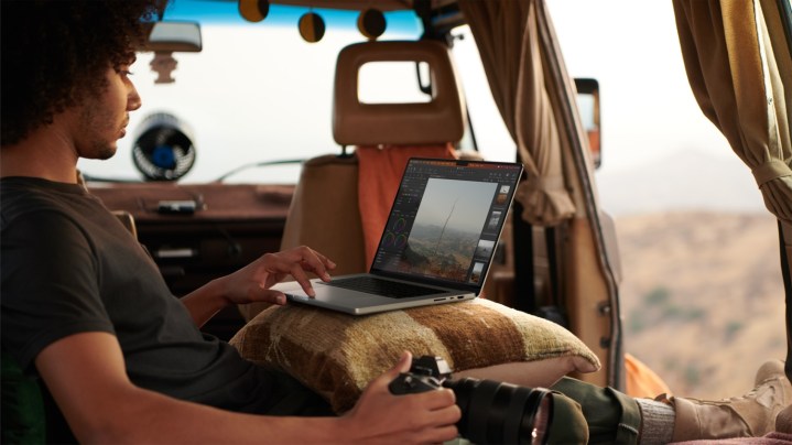 A person seated in a vehicle using a MacBook Pro on their lap.