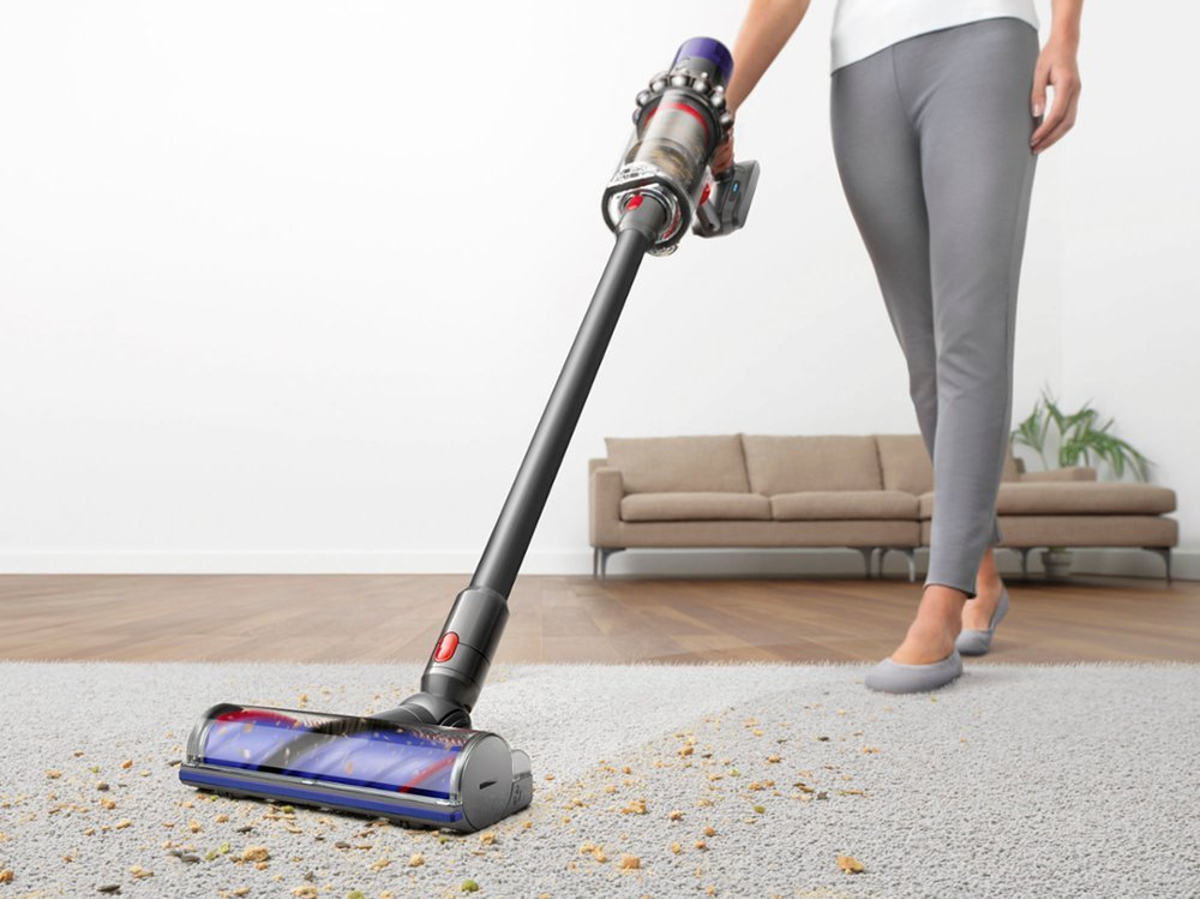 Cleaning a living room carpet with a mess of crumbs using a Dyson Cyclone V10 Animal cordless stick vacuum.