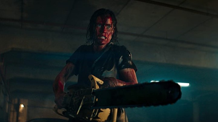 Uma mulher com o rosto ensanguentado segura uma motosserra em uma cena de Evil Dead Rise.