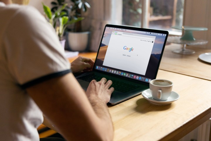 A person on the Google home page while using a MacBook Pro laptop on a desk.