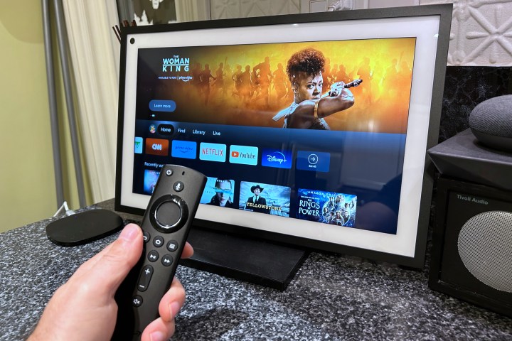 Amazon Echo Show 15 showing the Fire TV experience, with an Amazon Fire TV voice remote in the foreground.