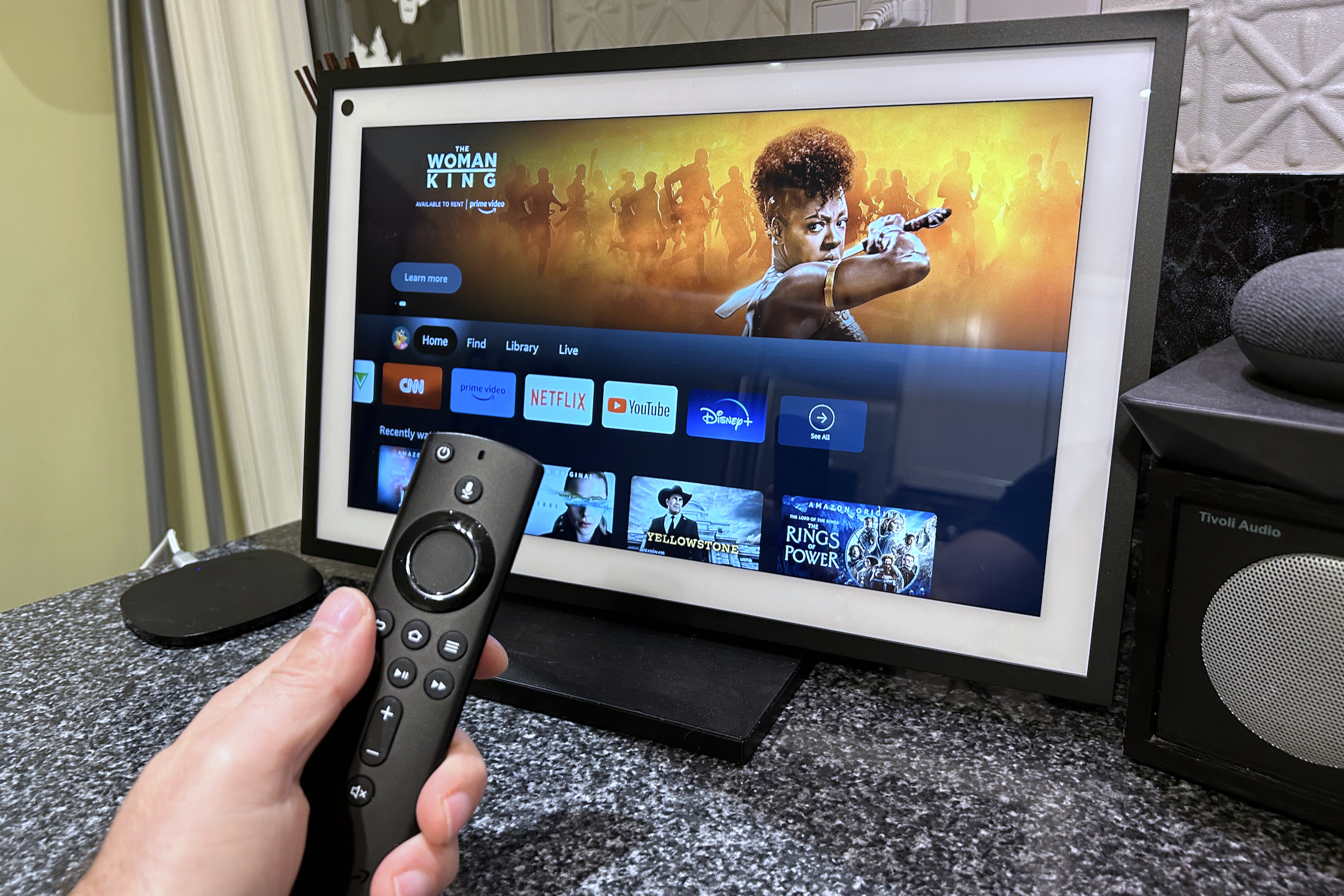 Amazon Echo Show 15 mostrando a experiência Fire TV, com um controle remoto de voz Amazon Fire TV em primeiro plano.