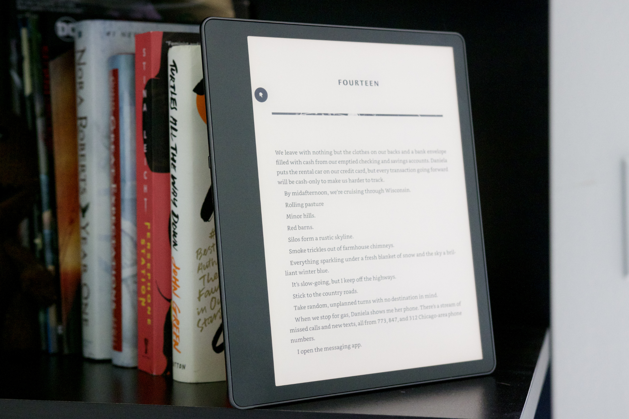 Amazon Kindle Scribe em uma estante ao lado de uma pilha de livros.
