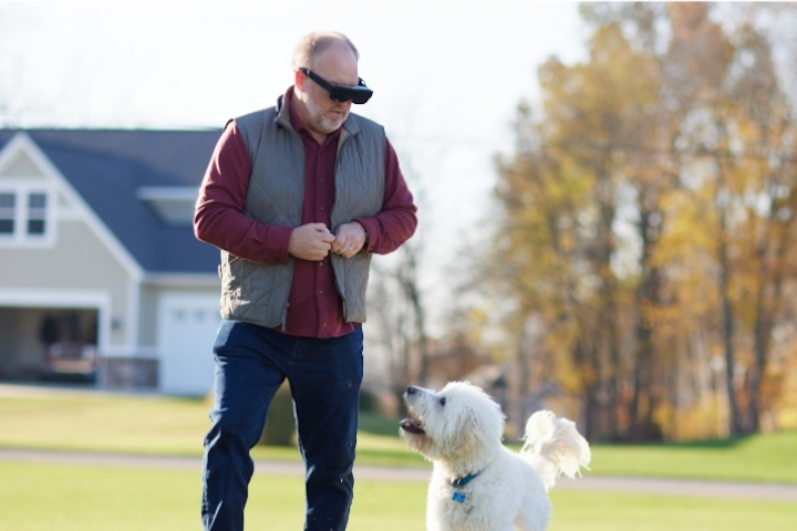 Homem usando eSight Go, passeando com um cachorro.