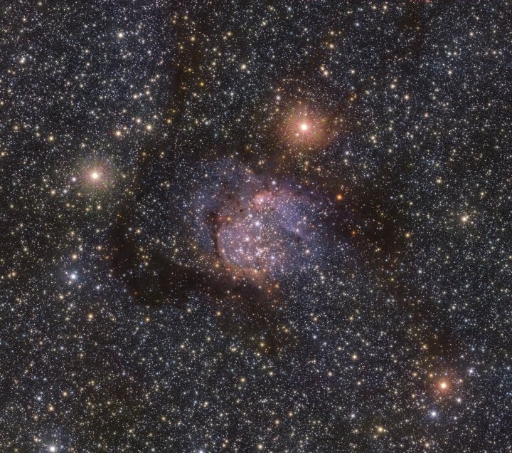 Esta imagen de la espectacular nebulosa Sh2-54 fue tomada en luz infrarroja utilizando el telescopio VISTA de ESO en el Observatorio Paranal en Chile. Las nubes de polvo y gas que normalmente son obvias en la luz visible son menos evidentes aquí, y en esta luz podemos ver la luz de las estrellas detrás de las nebulosas que ahora perforan.