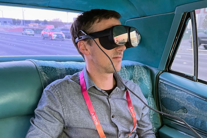The author wears an HTC Vive Flow VR headset in the back of a vintage Cadillac.