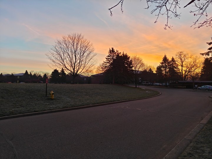 Photo of a sunrise against apartment buildings and trees.