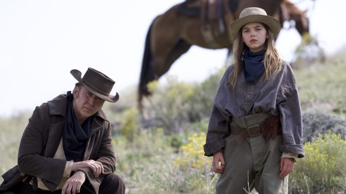 Nicolas Cage and Ryan Kiera Armstrong stand at the camera with a horse behind them in a scene from The Old Way.