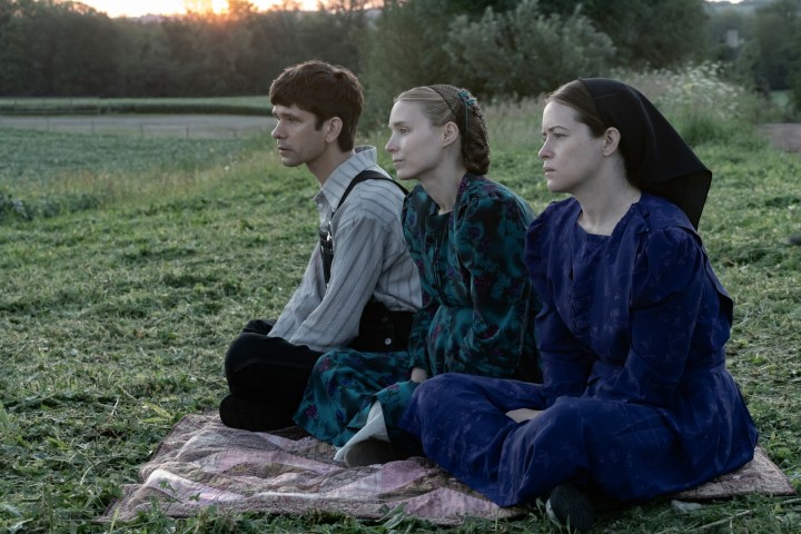 Two women and a man sit on grass in Women Talking.