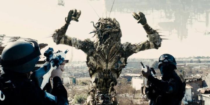 An alien holds up his hands with police aiming their guns at him in District 9.
