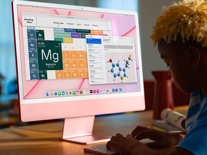 دانش آموزی پشت میز روی یک رایانه رومیزی 24 اینچی Apple iMac M1 روی میز می نویسد.
