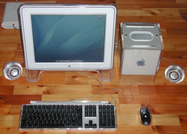 An Apple Power Mac G4 Cube computer on a desk next to an Apple monitor, keyboard, mouse and speakers.