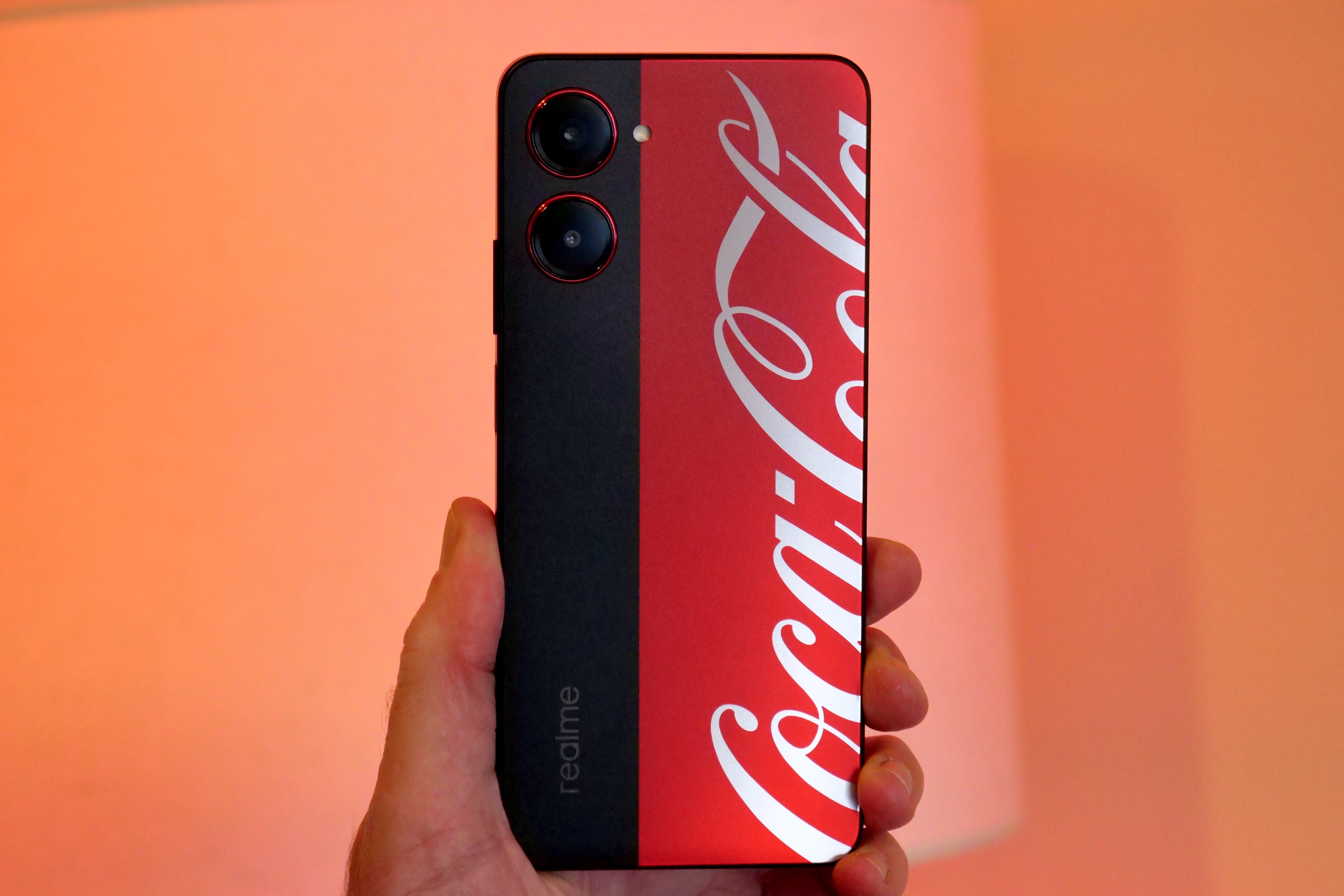 The Realme X Coca-Cola phone held in a person's hand, and seen from the back.