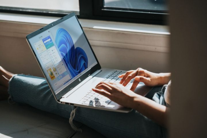 Person using Windows 11 laptop on their lap by the window.