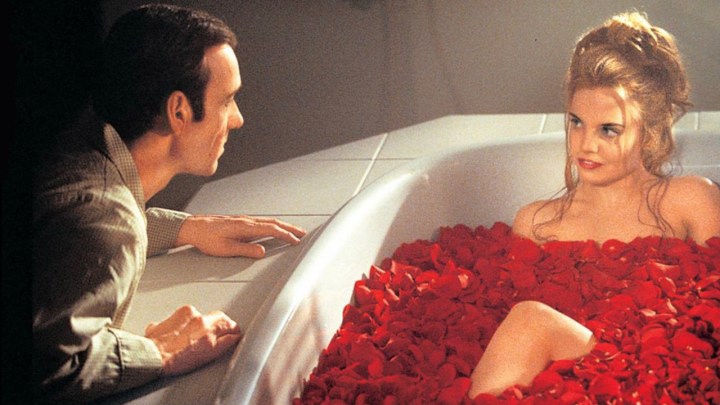 Kevin Spacey agachado junto a una niña en una bañera, cubierto de pétalos de rosa en una escena de American Beauty.