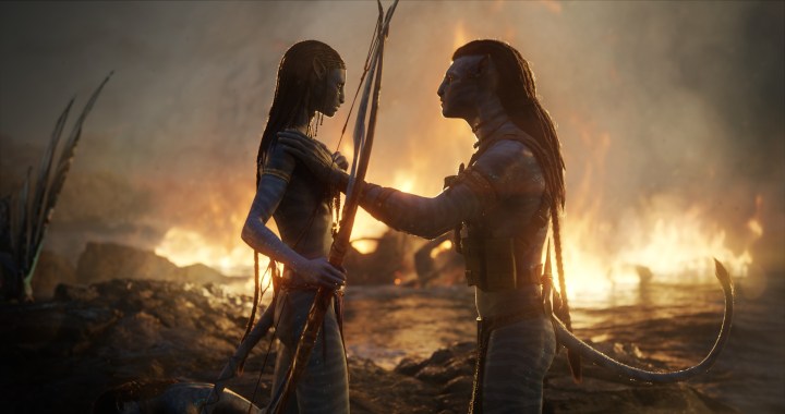 A pair of Na'vi comfort each other in the water while flames spread around them in a scene from Avatar: The Way of Water.