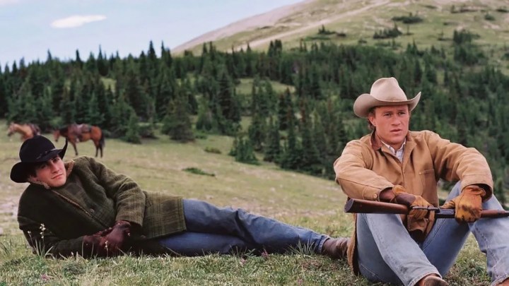 Jake Gyllenhaal lying on the grass, Heath Ledger sitting in front in a scene from Brokeback Mountain.