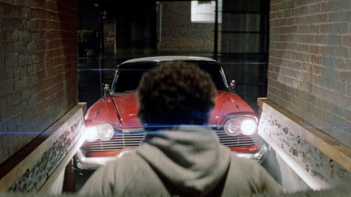 Um homem está na frente de um carro vermelho em Christine.