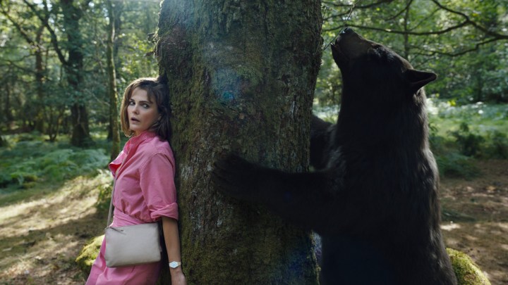 Keri Russell hides behind a tree as a bear tries to climb it in a scene from Cocaine Bear.