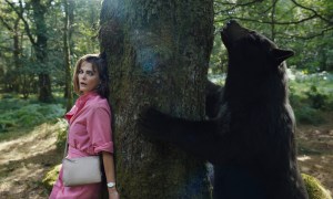Keri Russell hides behind a tree as a bear tries to climb it in a scene from Cocaine Bear.