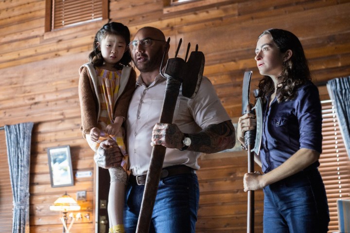 Kristen Cui is held by Dave Bautista, while Abby Quinn stands nearby with a crude weapon.
