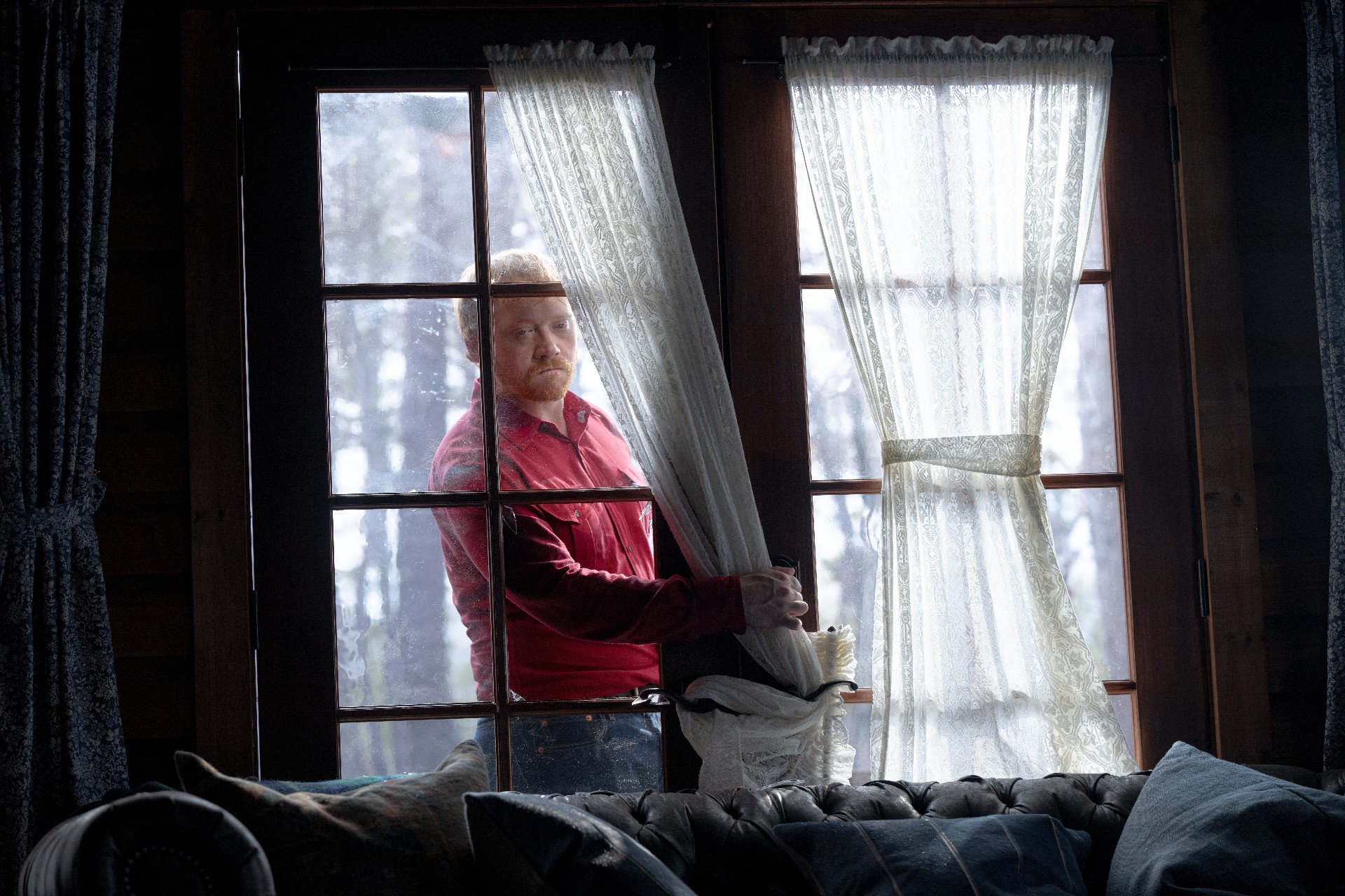 Rupert Grint enfia a mão por uma porta quebrada em uma cena de Knock at the Cabin.
