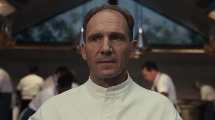 Ralph Fiennes em uma jaqueta de chef parecendo irritado em uma cena de The Menu.