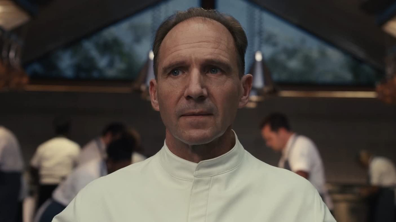 Ralph Fiennes in a chef's jacket looking angered in a scene from The Menu.