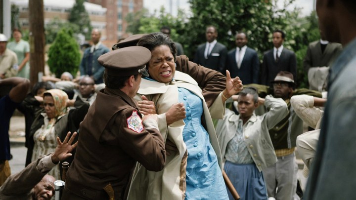 Oprah Winfrey in a scene from Selma, being restrained by authorities, a crowd behind her.