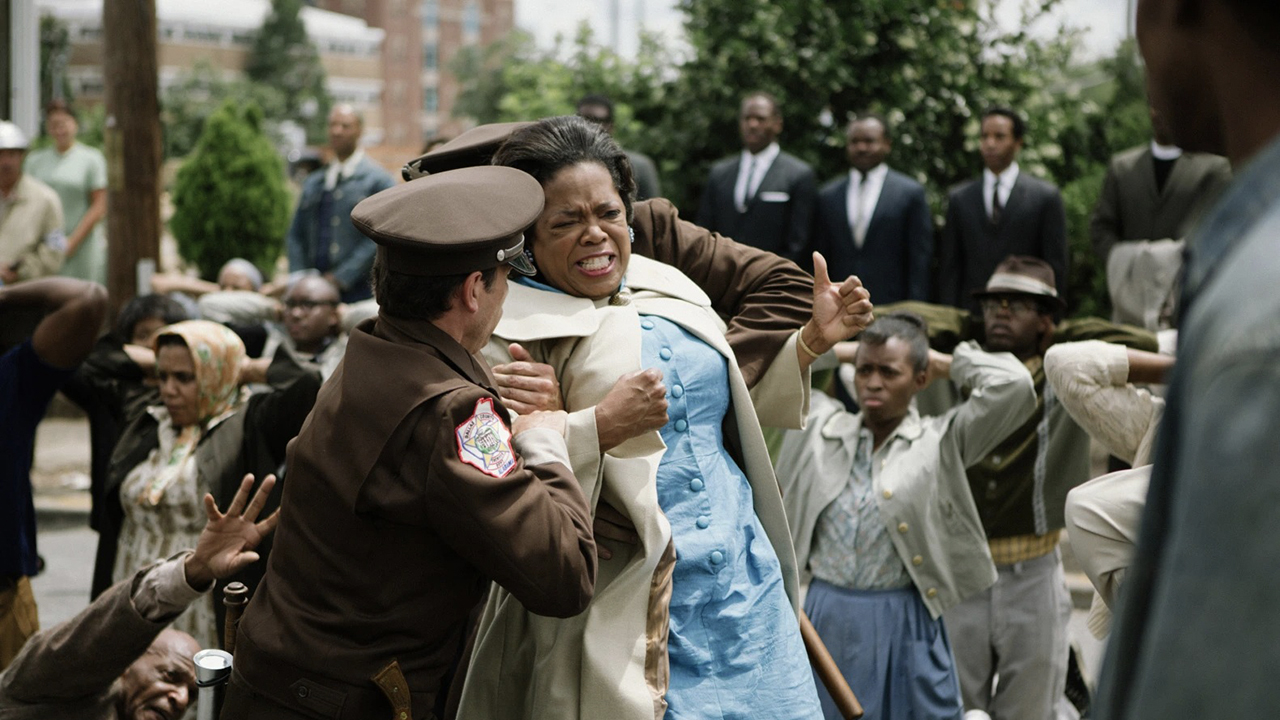 Oprah Winfrey em cena de Selma, sendo contida pelas autoridades, uma multidão atrás dela.