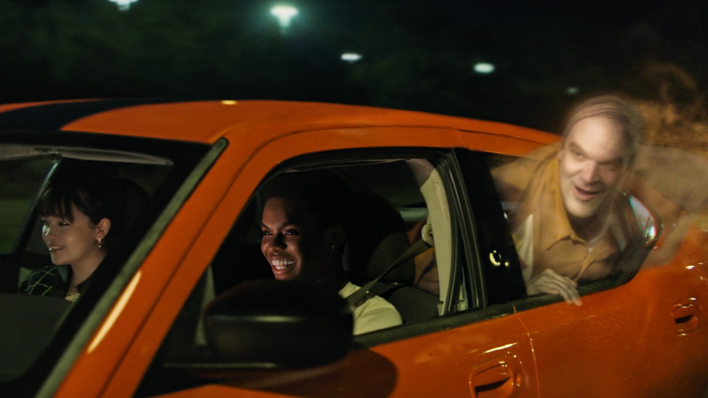 Um fantasma transparente interpretado por David Harbour coloca a cabeça para fora da janela de um carro em uma cena de We Have A Ghost.