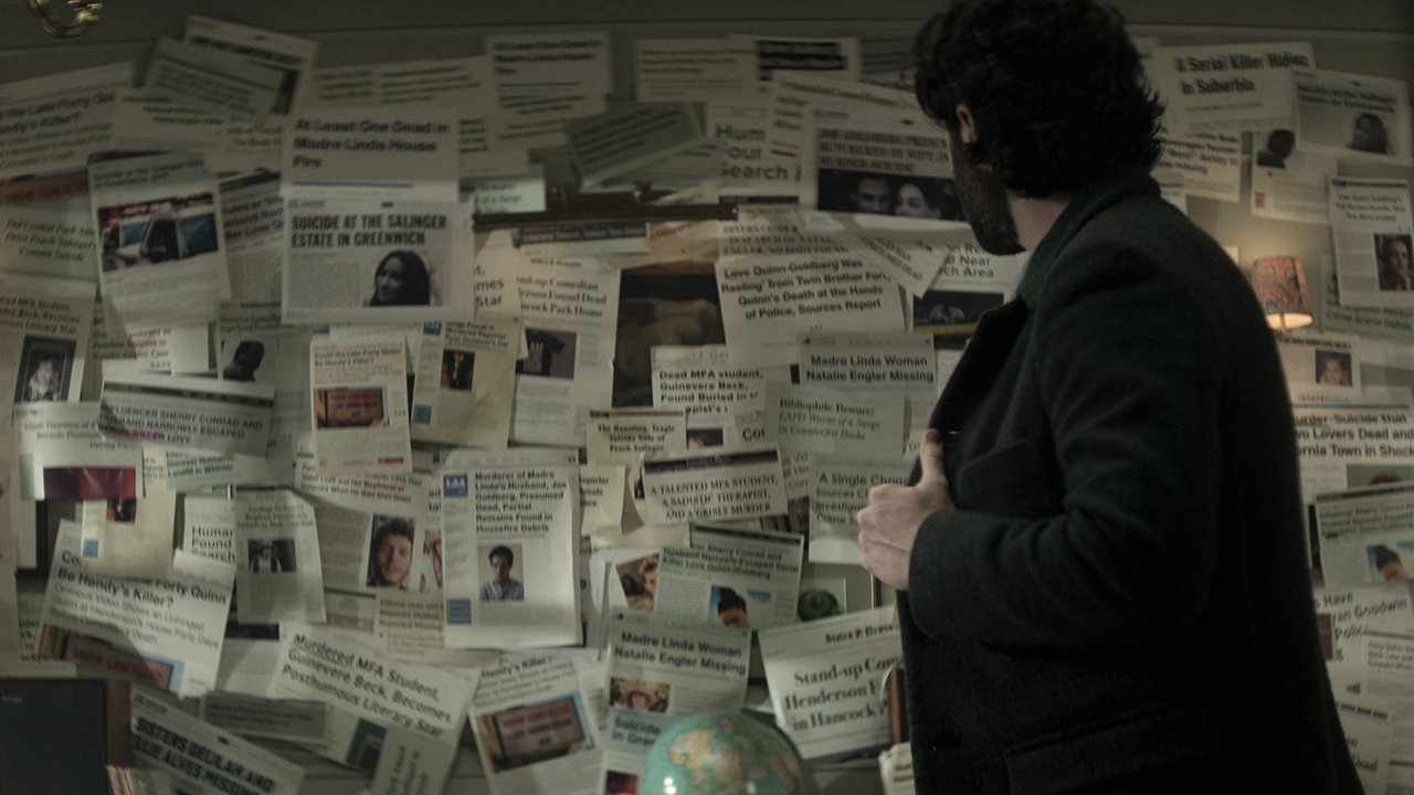 Joe de You olhando para uma colagem de artigos de jornais antigos em sua parede na 4ª temporada.