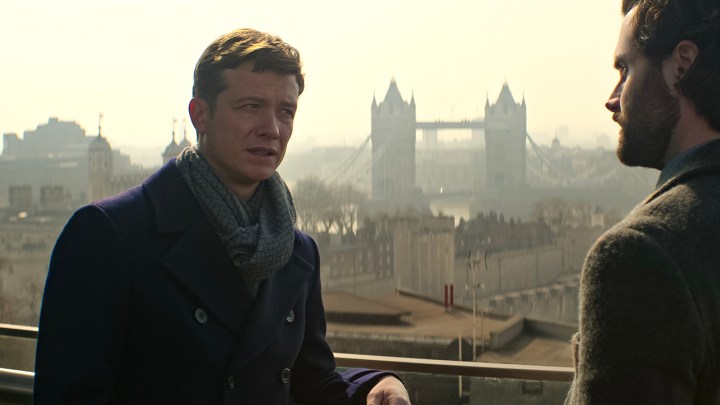 Rhys standing on a balcony talking to Joe in a scene from You Season 4.