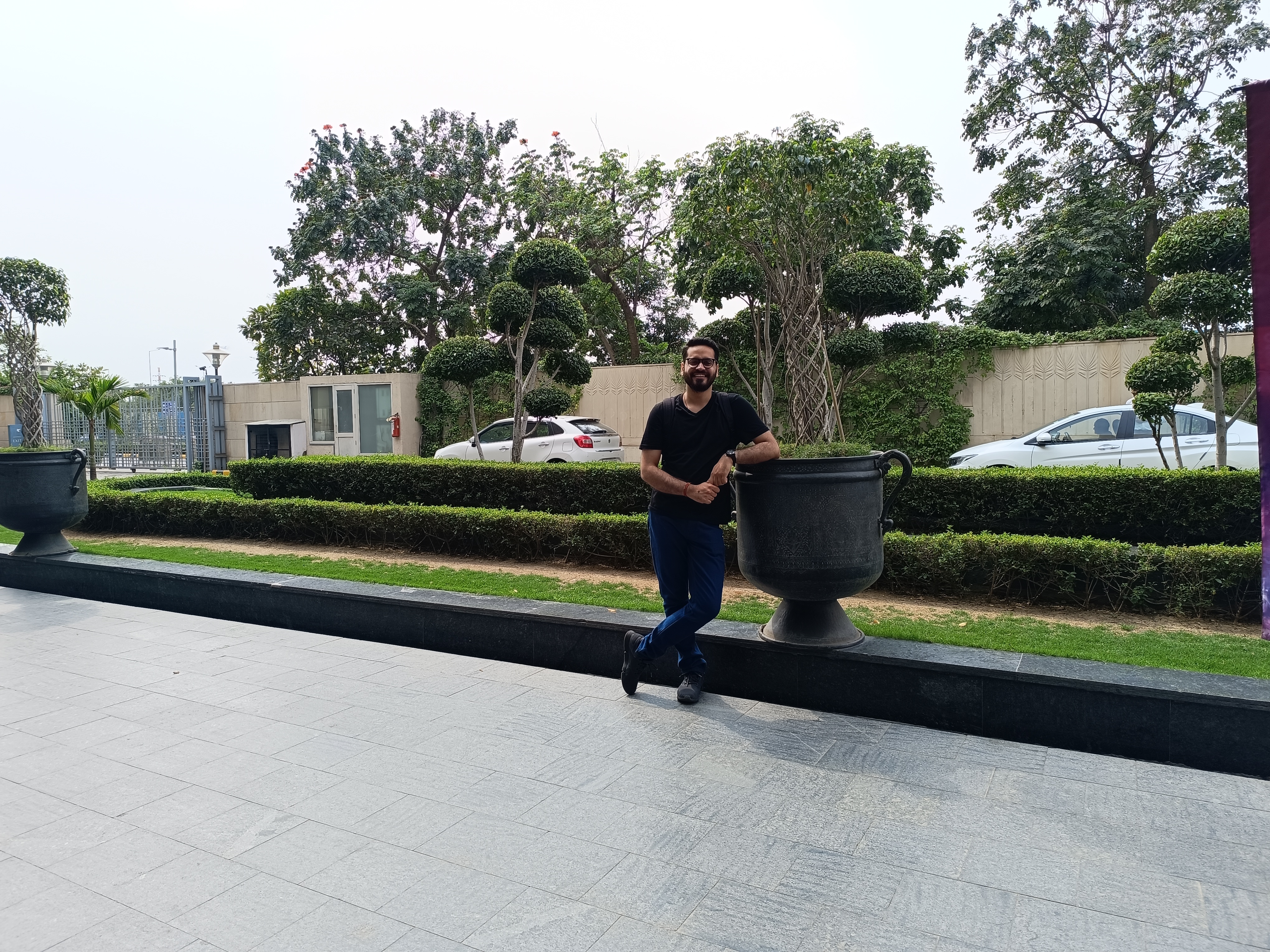 Man leaning againt a large vase in a hotel driveway captured by Redmi Note 12 Pro Plus.