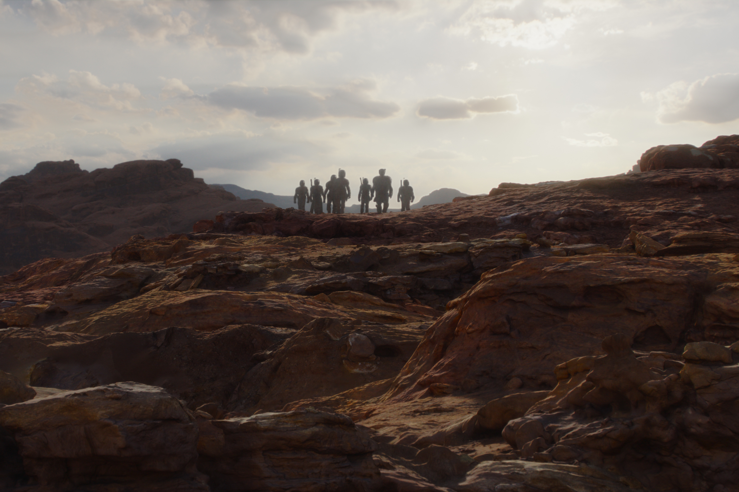 Um grupo de Mandalorianos caminha em um planeta rochoso na terceira temporada de The Mandalorian.