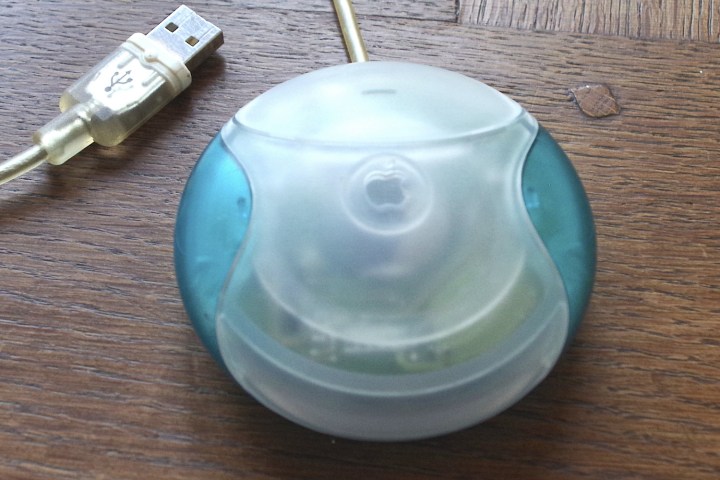 Apple USB Mouse, commonly known as "Hockey disc" Mouse, from iMac G3.  The mouse is sitting on a desk with a USB cable next to it.