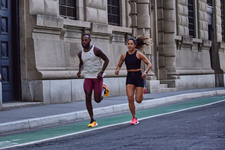 Two people running on a city street wearing Garmin Forerunner 965 and 265 smartwatches.