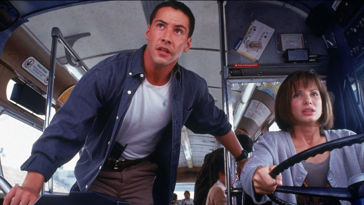 Keanu Reeves stands next to a bus driver in Speed.