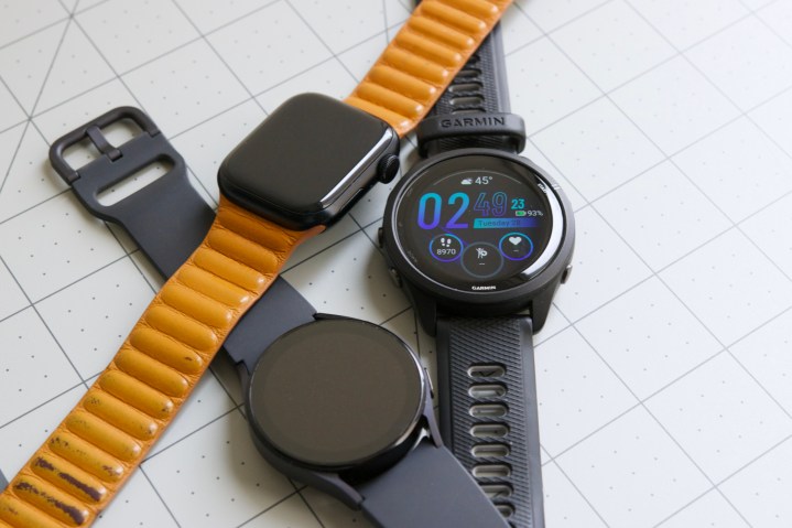 An Apple Watch, Galaxy Watch 5, and Garmin Forerunner 265 lying on a desk next to each other.