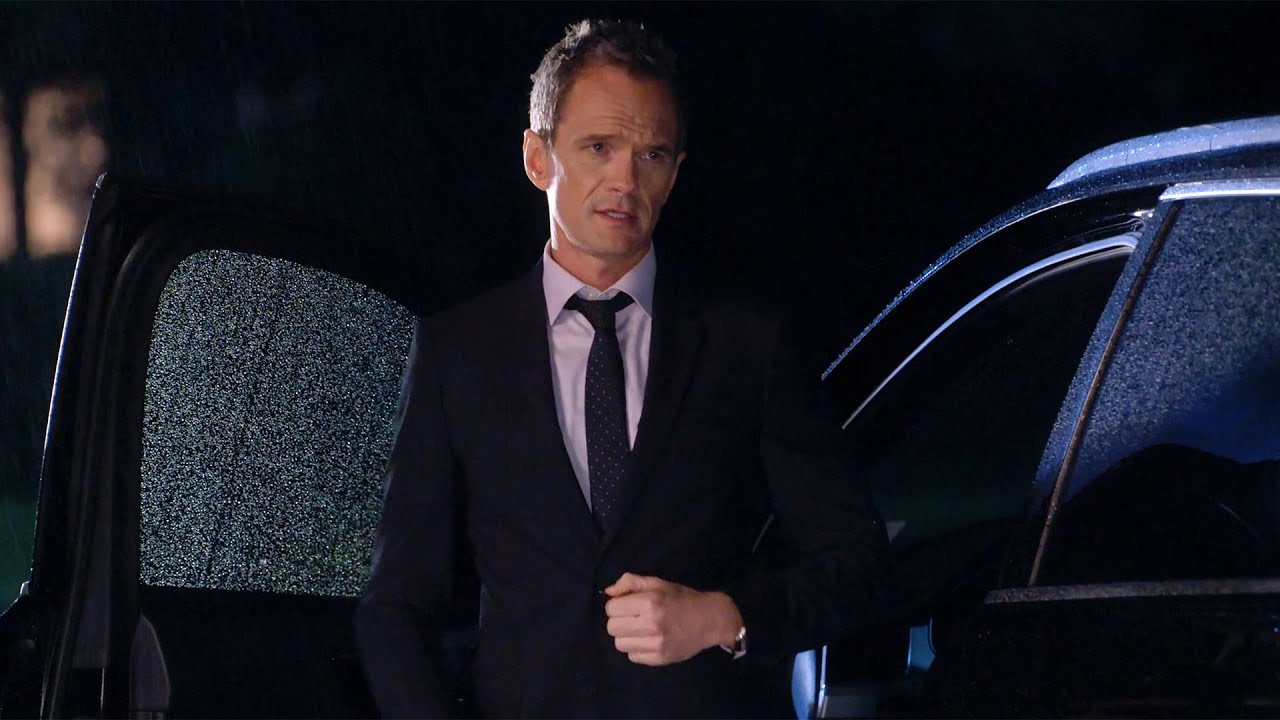 Barney segurando o botão do paletó parado na frente do carro em uma cena de How I Met Your Father.
