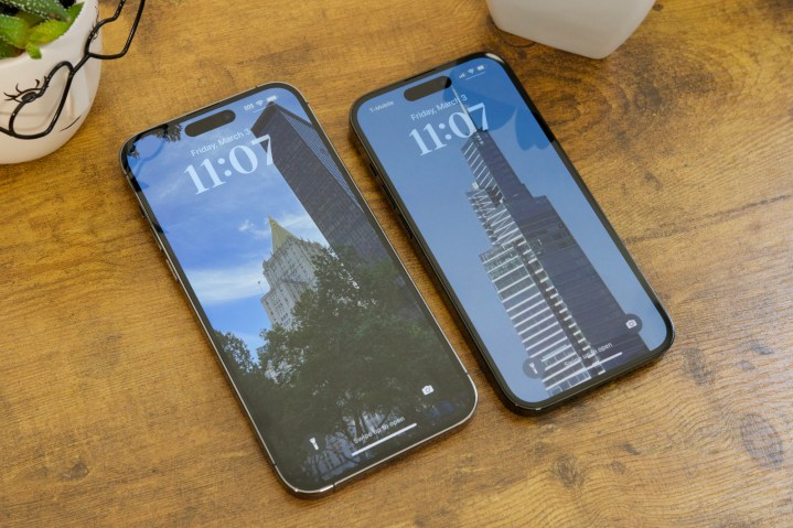 An iPhone 14 Pro Max and iPhone 14 Pro laying on a table with their screens on.