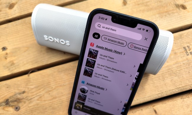 An iPhone 14 displaying the Sonos app search feature, sitting in front of a Sonos Roam speaker.