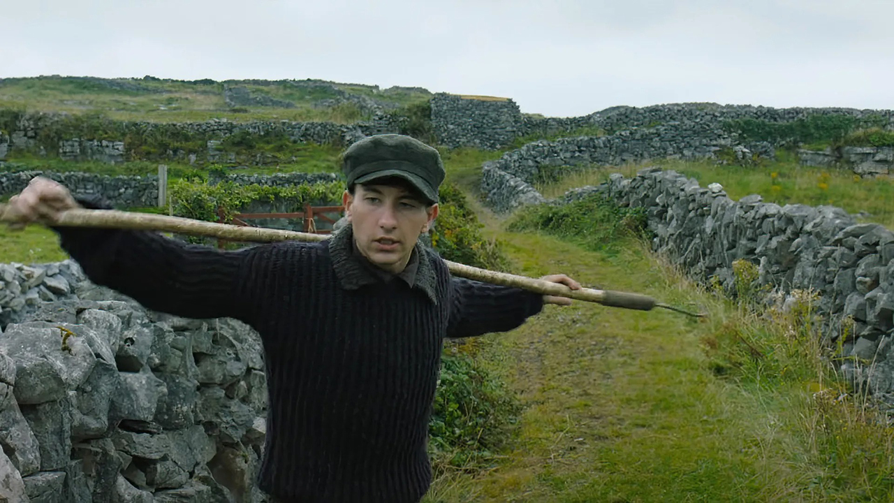 Barry Keoghan em The Banshees of Inisheran, segurando um poste nas costas, parado em um campo.