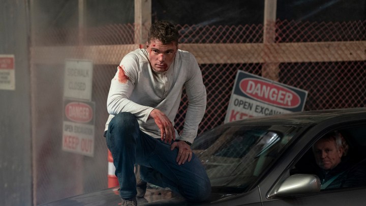 Peter ajoelhado em cima de um carro, ensanguentado e espancado em uma cena de The Night Agent.