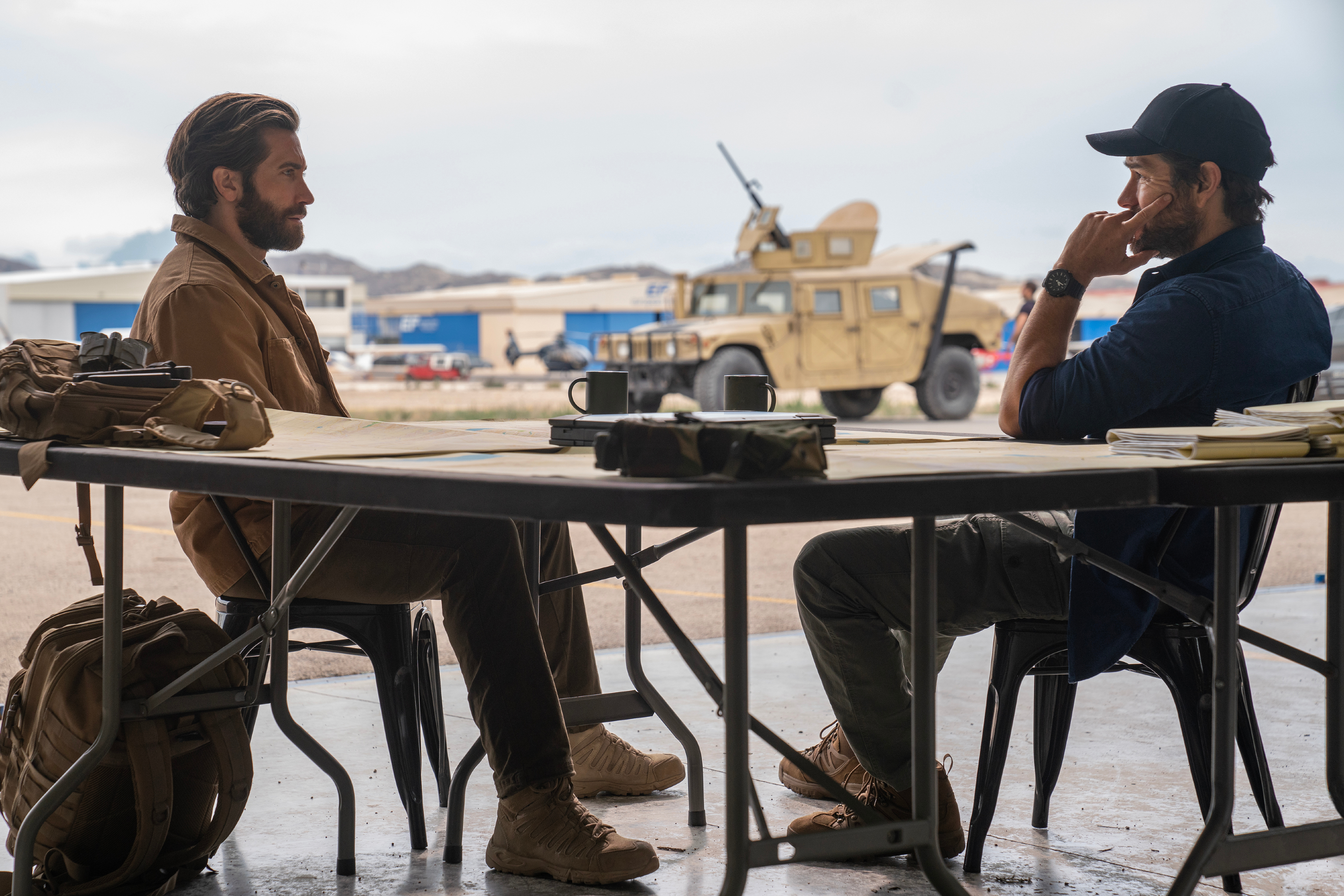 Jake Gyllenhaal e Antony Starr olham um para o outro através de uma mesa em The Covenant, de Guy Ritchie.