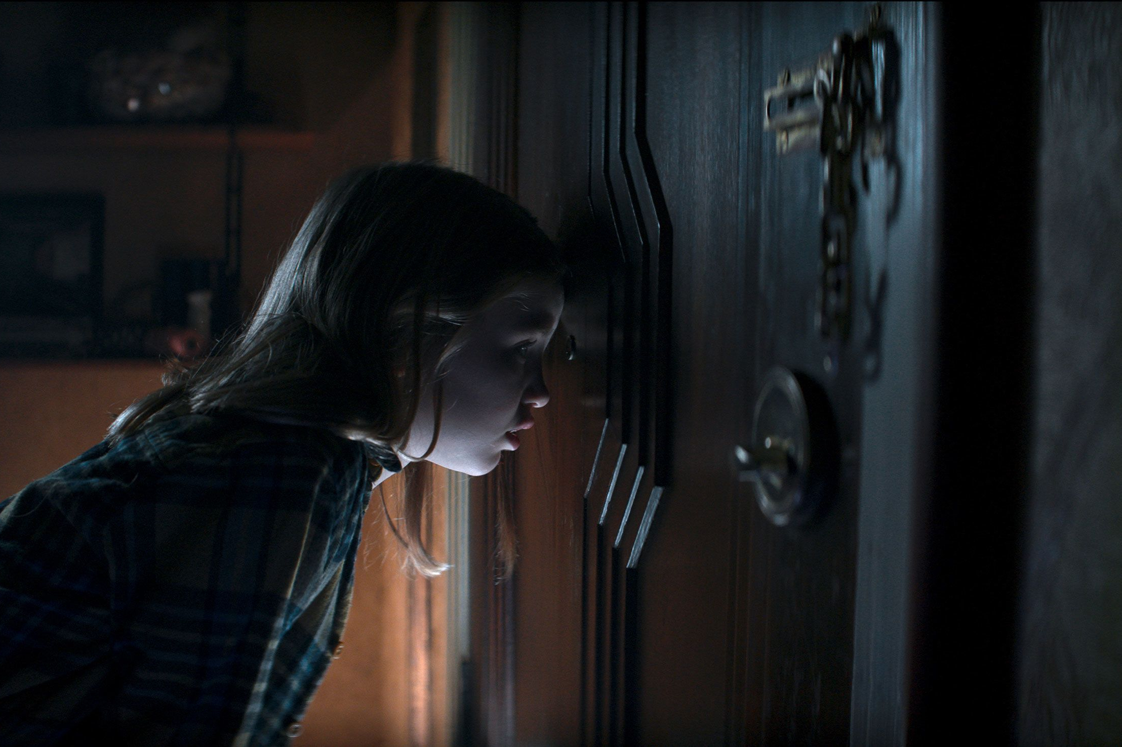 Kassie olha pelo olho mágico de uma porta em Evil Dead Rise.