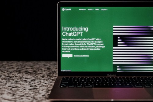 The ChatGPT website on a laptop's screen as the laptop sits on a counter in front of a black background.