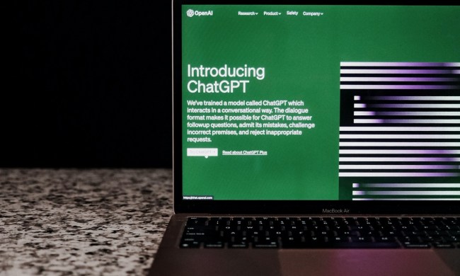 The ChatGPT website on a laptop's screen as the laptop sits on a counter in front of a black background.