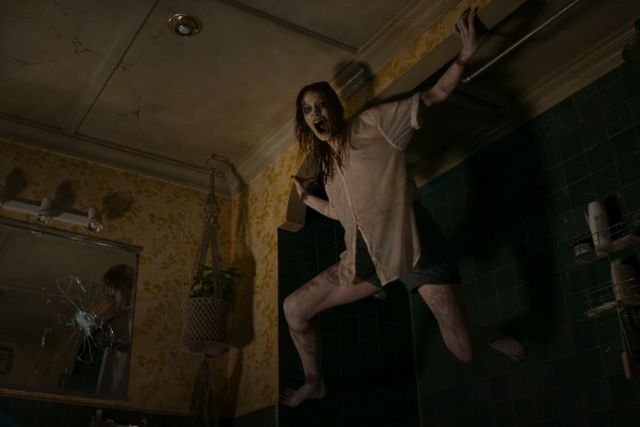 Undead Ellie holds herself up near her bathroom ceiling in Evil Dead Rise.