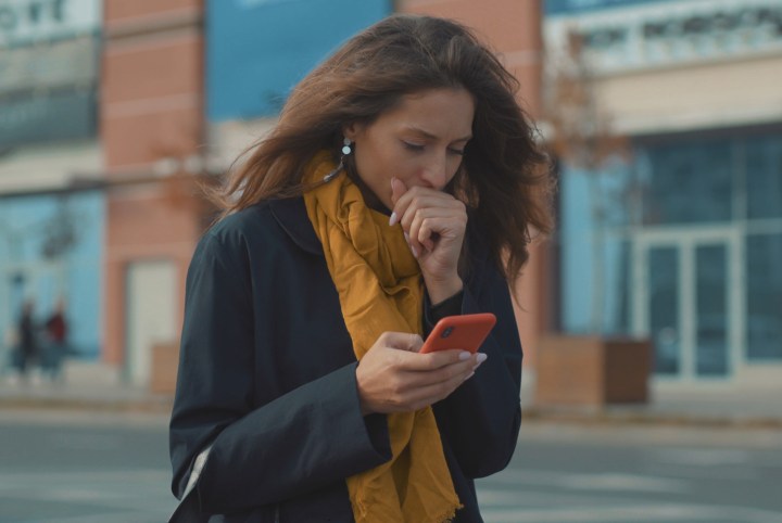 A woman coughing and holding a smartphone.